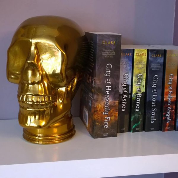 AMP3 glass skull headphone stand, gold, on a bookshelf